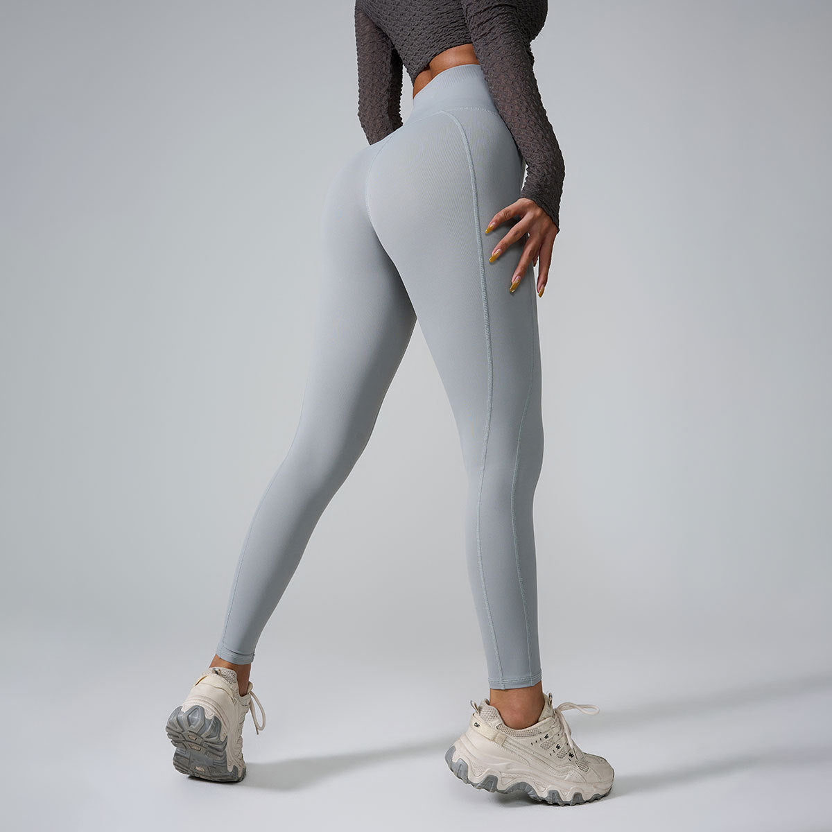 A model wearing light gray high-waisted leggings with textured crop top, showing side view profile against gray backdrop