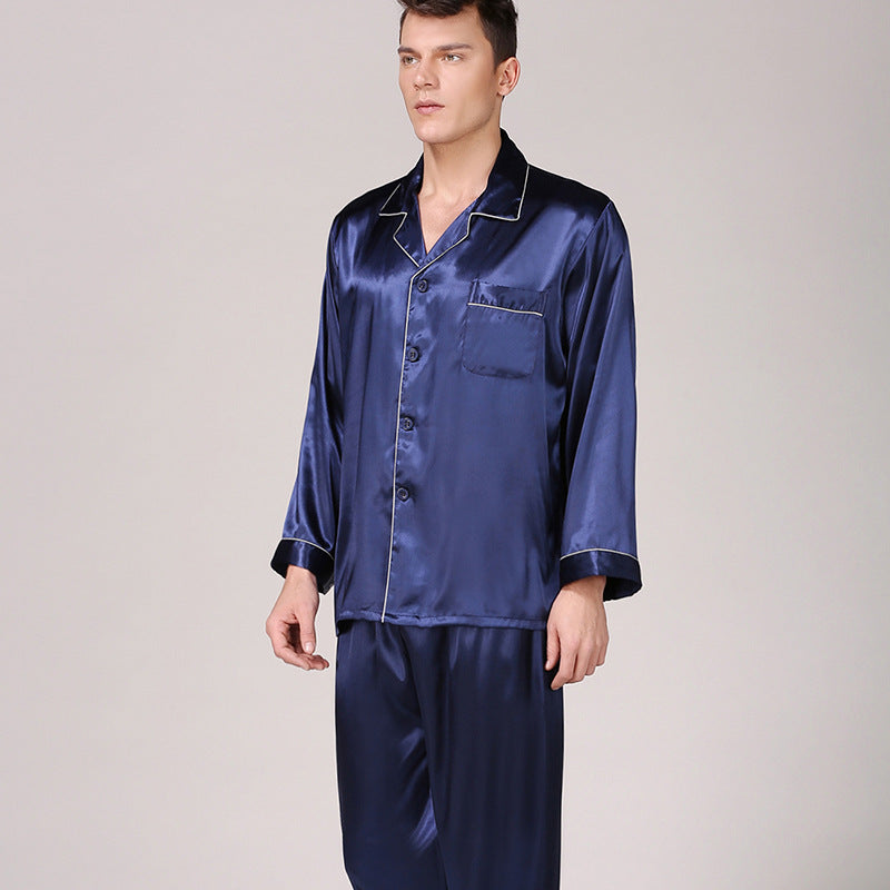 Side angle of man wearing navy blue satin pajamas with white piping detail and chest pocket