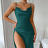 Woman in a green satin slip dress with a thigh-high slit, standing near a bed