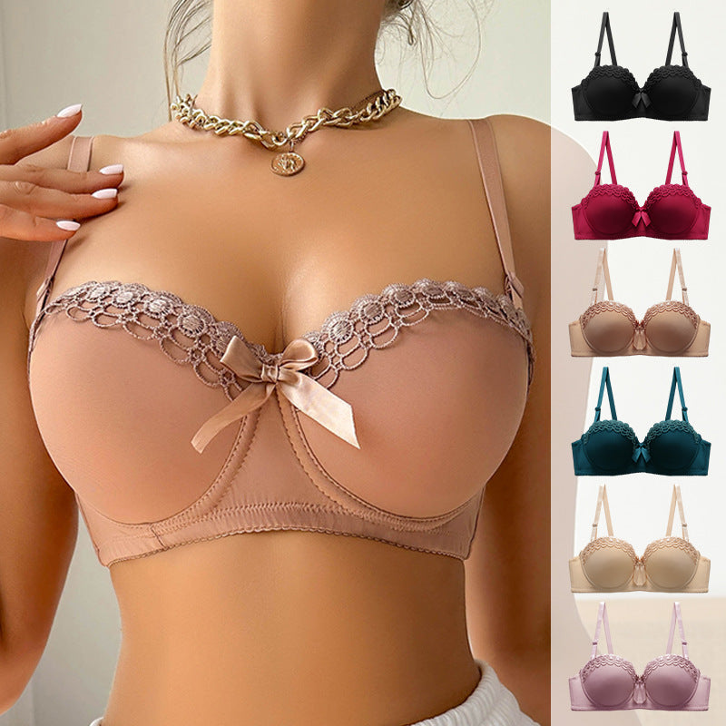 A woman wearing a nude/beige push-up bra with lace trim and gold chain necklace with pendant against white background