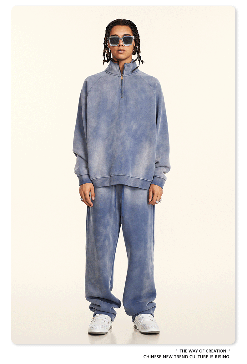 Model wearing blue tie-dye quarter-zip sweatshirt and matching joggers with white sneakers against cream background