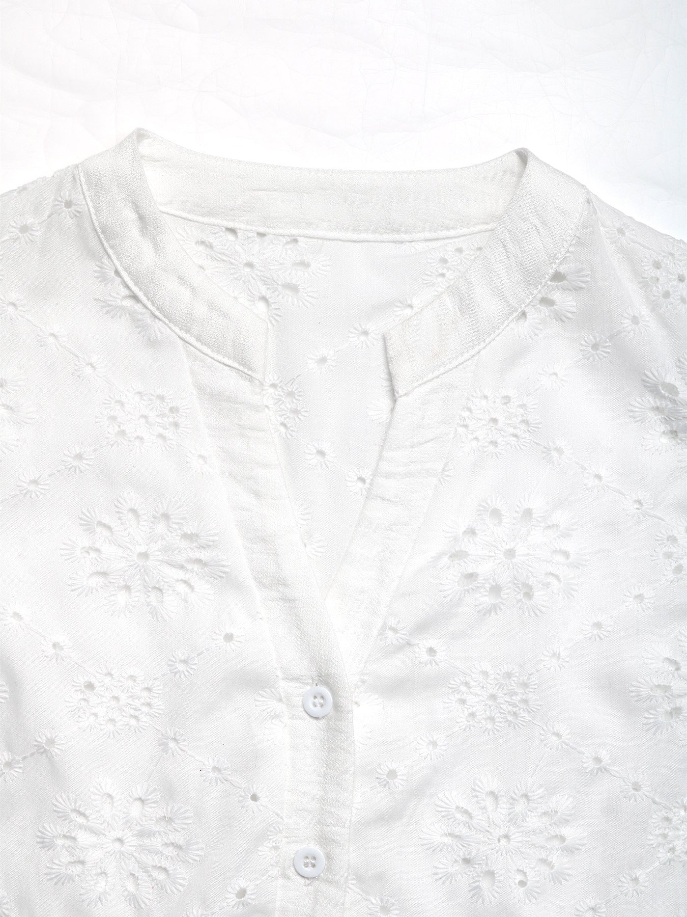 Close-up of V-neck button-up design on white embroidered blouse, highlighting fine stitching and delicate lace detailing.
