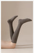 Artistic photo of gray knee-high socks on crossed legs against beige background