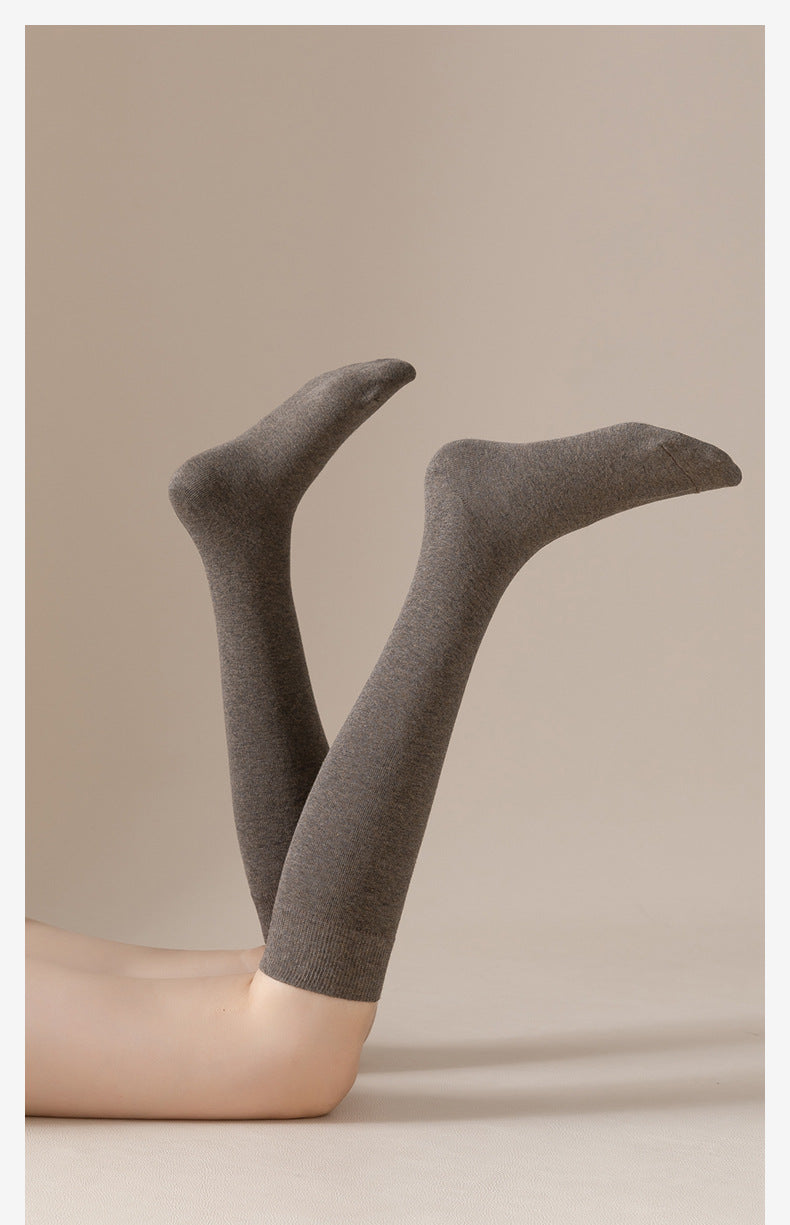 Artistic photo of gray knee-high socks on crossed legs against beige background