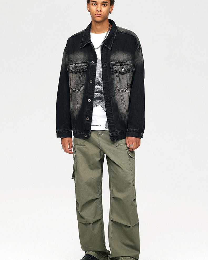 A man wearing black faded denim jacket over white graphic tee and olive cargo pants with chunky black boots against white backdrop