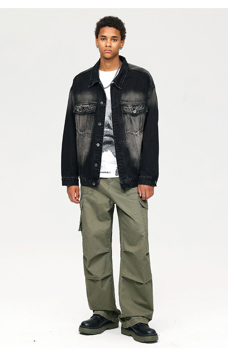 A man wearing black faded denim jacket over white graphic tee and olive cargo pants with chunky black boots against white backdrop