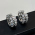 Silver huggie hoop earrings with filigree design and crystal rows on black display surface