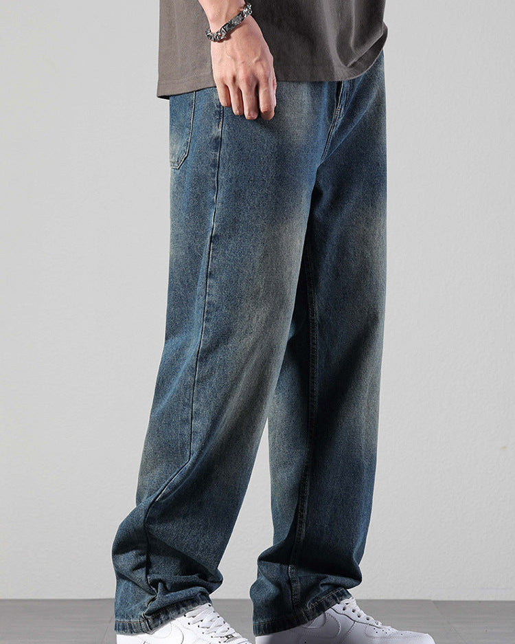 A person wearing relaxed fit vintage wash jeans with gray oversized t-shirt and metal chain bracelet, standing in white Nike Air Force 1 sneakers