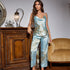 Light blue satin pajama set with soft floral print, including a camisole top and wide-leg pants, styled near antique furniture
