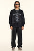 Full-length shot of model in matching black sweatshirt and wide-leg sweatpants, Winding Decoration graphic, white sunglasses, silver jewelry, animal print sneakers