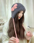 Gray fuzzy winter hat decorated with pink crochet bow and matching pink braided ties
