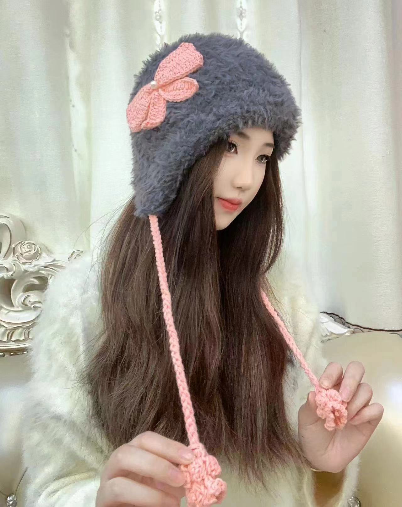 Gray fuzzy winter hat decorated with pink crochet bow and matching pink braided ties
