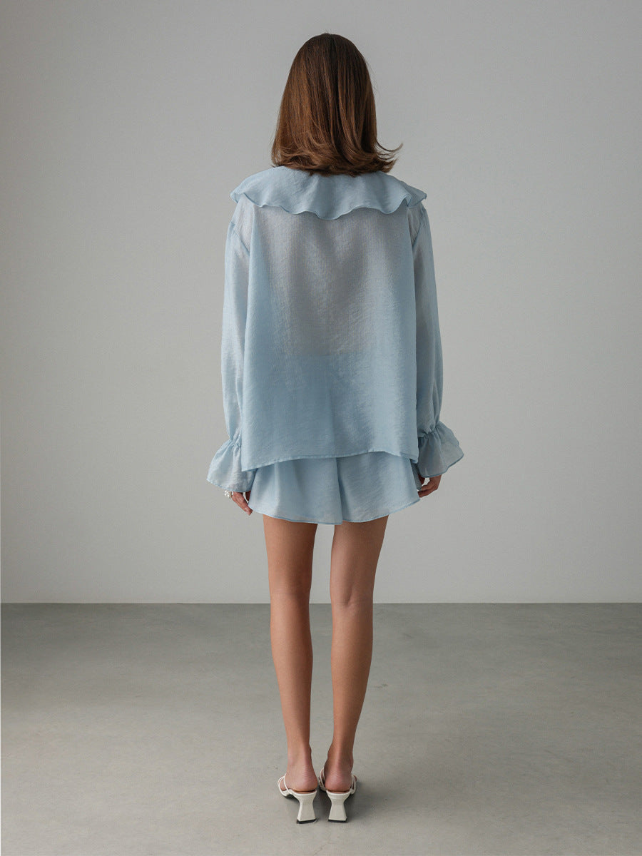 Woman wearing a light blue outfit with ruffled details against a plain background