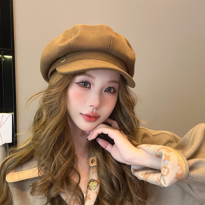 Woman with camel newsboy cap with hand on chin, wearing matching beige jacket with designer accent buttons