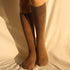 Side angle view of person wearing knee-high brown cotton socks against cream background in warm sunlight
