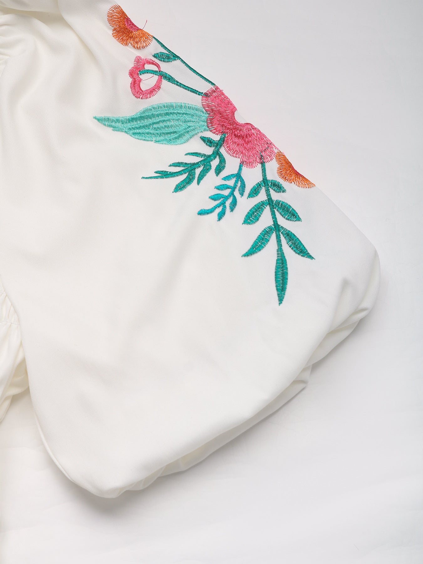 Detailed view of the embroidered floral design on the puff sleeve of the white blouse.