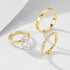 Three gold rings displayed together: oval diamond solitaire, eternity band with small diamonds, and thin band with flower-shaped diamond accents