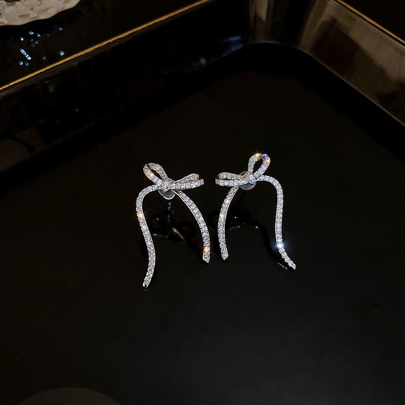 Elegant silver bow earrings with crystal pavé detail shown on black surface, emphasizing symmetrical design
