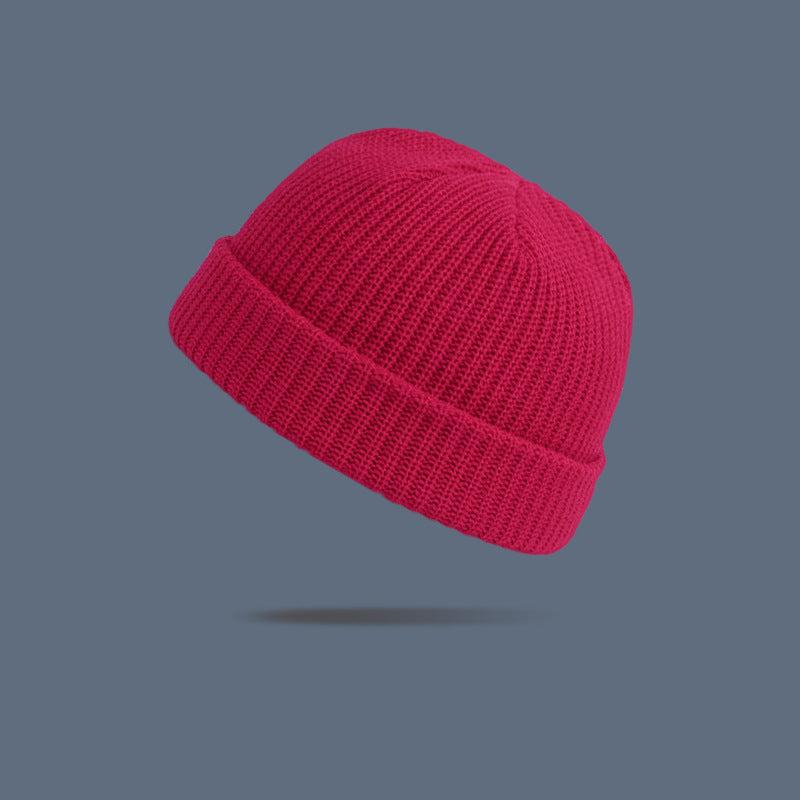A bright fuchsia ribbed knit beanie with folded cuff floating against slate gray background, showing vibrant winter accessory