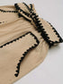 Detailed side view of beige high-waisted shorts with intricate black lace trim outlining the pockets and hem.