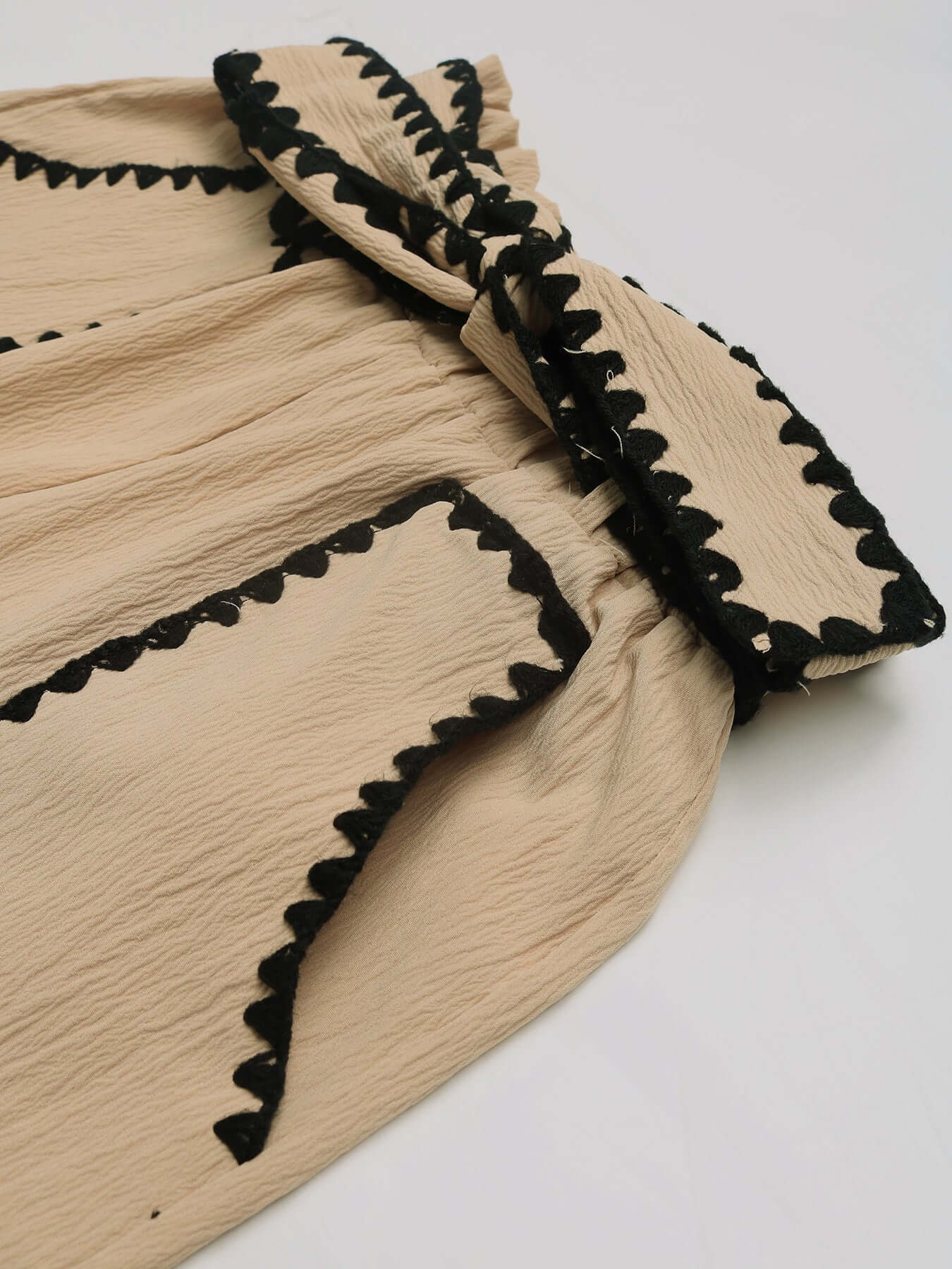 Detailed side view of beige high-waisted shorts with intricate black lace trim outlining the pockets and hem.
