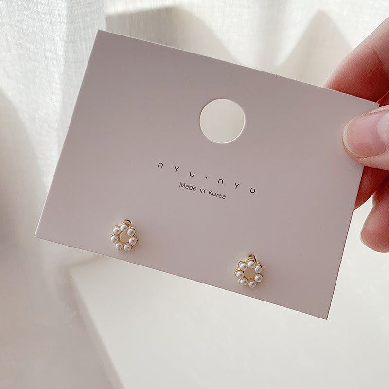 A pair of small gold stud earrings with a circular arrangement of tiny pearls, displayed on a white card