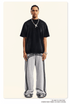 A man wearing oversized black t-shirt and light gray sweatpants with double side stripes stands against neutral background, accessorized with silver chain necklace