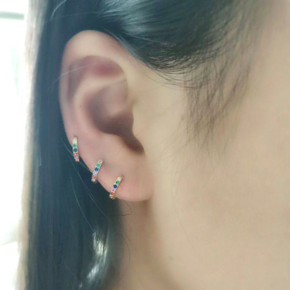 A woman wearing three rainbow gemstone huggie hoops along her earlobe creating a stacked effect