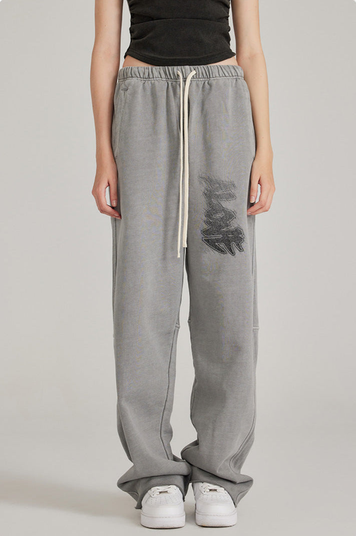 Close-up of grey sweatpants with elastic waistband, white drawstring and graffiti-style graphic print. Paired with black crop top