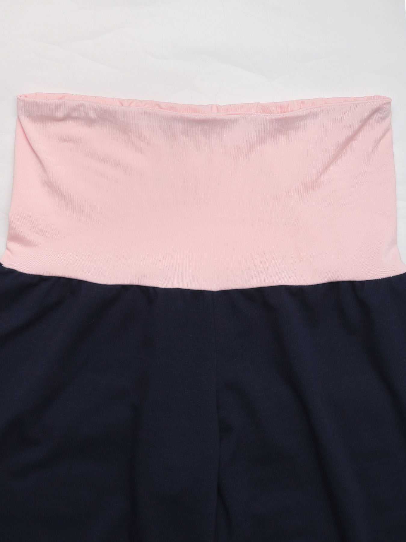 Detailed view of pink fold-over waistband on navy blue pants, showing the contrast color and smooth fabric.