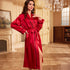 A woman in a red silk robe with black piping in an elegant room with crystal chandelier and ornate fireplace