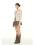 Side view of cream ribbed sweater with off-shoulder design, lace-up front detail, and distressed hem. Styled with brown suede pleated skirt, studded choker, and tall brown boots