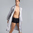 Man in silver patterned silk robe with white trim. Close-up shows open chest styling and black underwear against minimalist gray backdrop