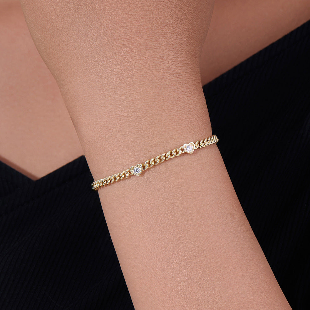 Gold heart charm bracelet worn on wrist, styled with a black top.