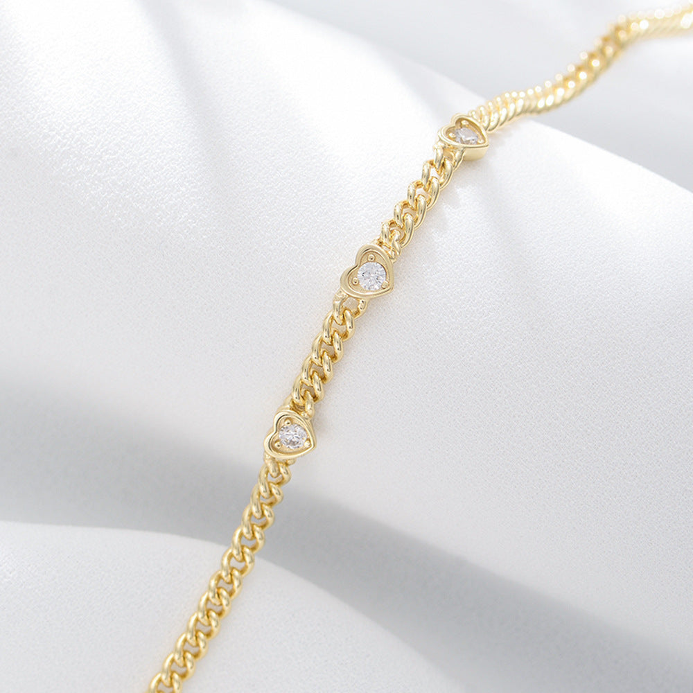 Close-up of gold bracelet on white fabric, highlighting heart-shaped CZ details.