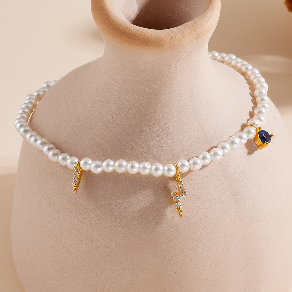 Pearl charm bracelet draped around a ceramic vase, featuring lightning bolts and a blue gem.