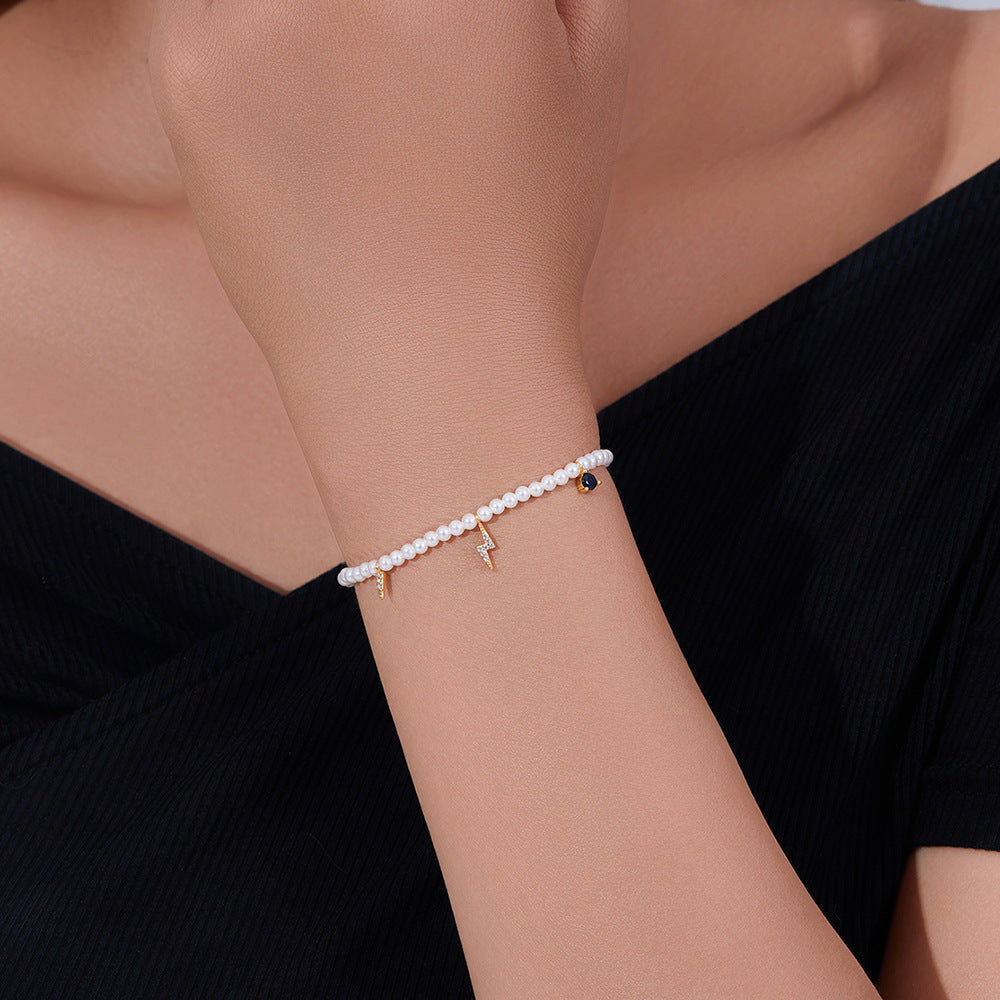 Woman wearing pearl bracelet with gold lightning bolt and sapphire-like heart charm.