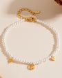 Gold-plated pearl bracelet with peace, heart, and star charms on cream background.
