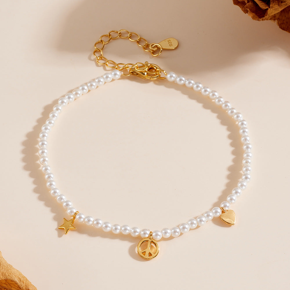 Gold-plated pearl bracelet with peace, heart, and star charms on cream background.