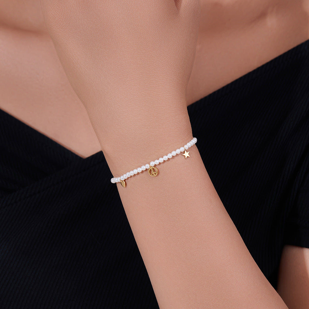 Model wears pearl bracelet with dangling gold peace, heart, and star charms.