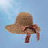 Brown woven straw sun hat with a red floral bow, wide brim, and breathable open-weave design, set against a blue sky background.