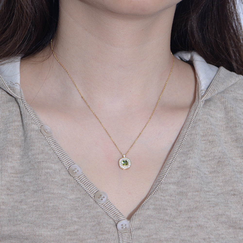 Woman wearing gold necklace with green CZ pendant, centered on chest over beige top.