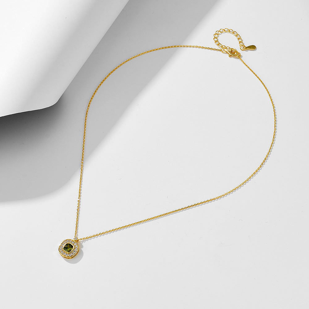  Full view of gold green CZ pendant necklace laid out on white surface in soft lighting.
