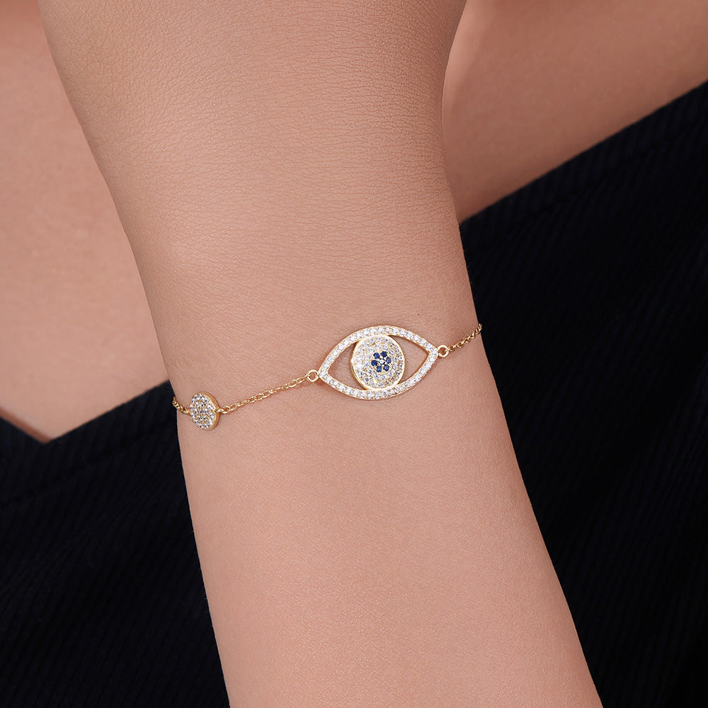 Woman wearing gold evil eye bracelet with central CZ eye charm.