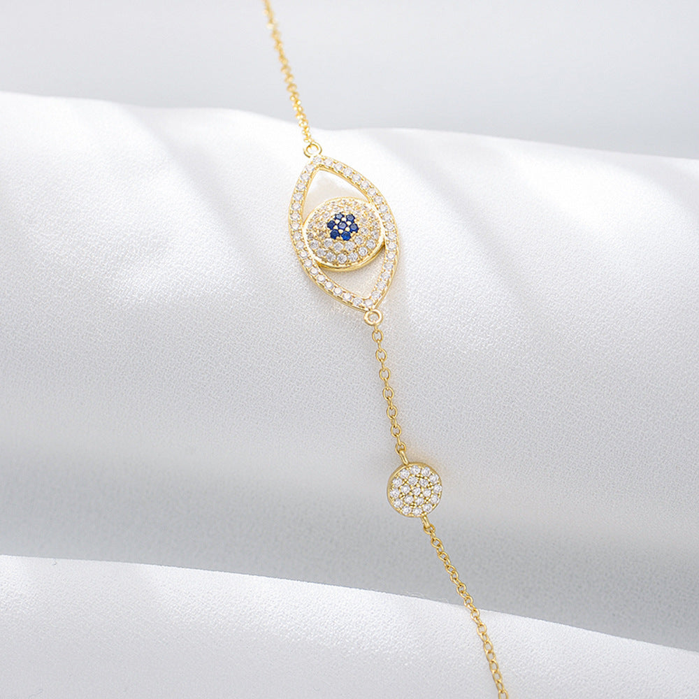 Gold evil eye bracelet displayed on white satin surface.
