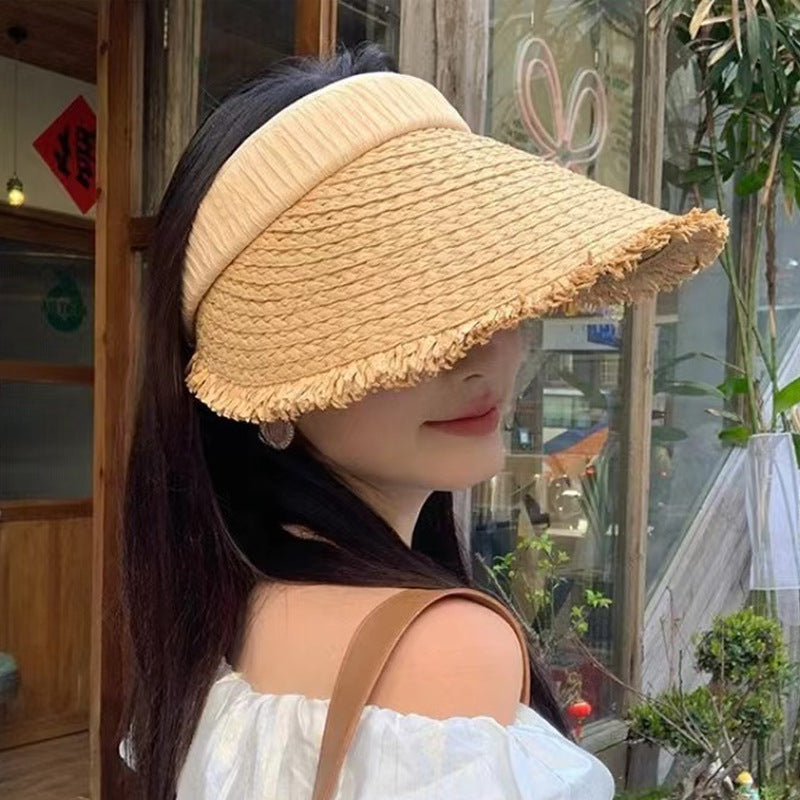 A woman wearing a beige straw visor hat with a soft band and wide frayed brim, paired with a white off-shoulder top for a chic look.