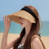 A woman at the beach wearing a straw visor with a black fabric band and frayed brim, shielding her face from the sun.
