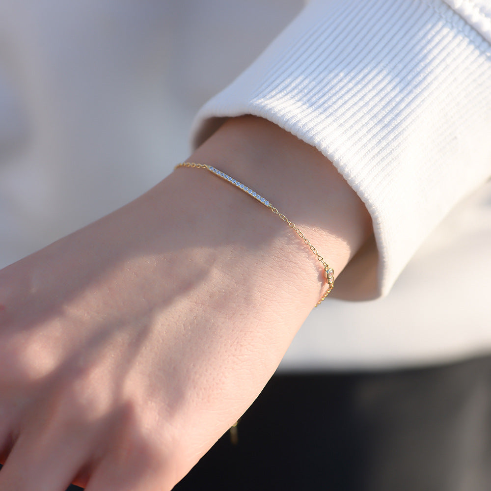 Close-up of gold bar bracelet on wrist in sunlight.