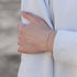 Gold bar bracelet worn on wrist with white long sleeve shirt.