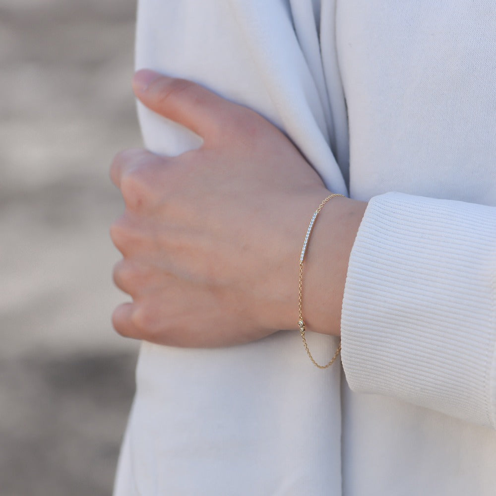 Gold bar bracelet worn on wrist with white long sleeve shirt.